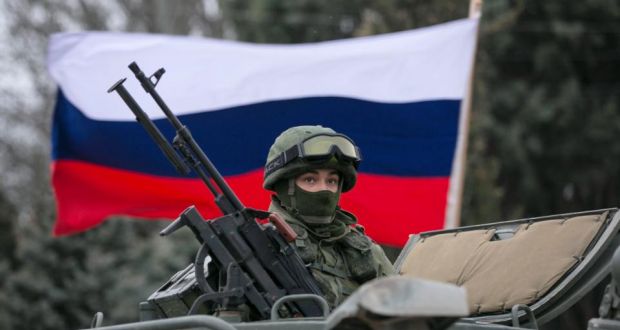 A Russian flag behind an armed servicemen on top of a Russian army vehicle outside a Ukrainian border guard post in the Crimean town of Balaclava today